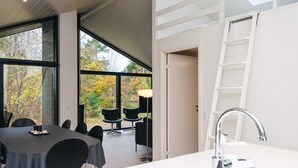 A modern kitchen with a stainless steel sink, a white countertop, and a view of the outdoors through large windows.