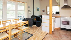 A cozy kitchen with a wood stove, white cabinets, and a dining area with wooden chairs and a table. - 6 Person Holiday Home in Laeso (Læsø)