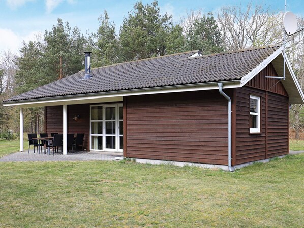 A wooden cabin with a covered patio, a chimney, and a satellite dish.