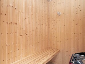 A wooden sauna room with a bench and a sauna heater.