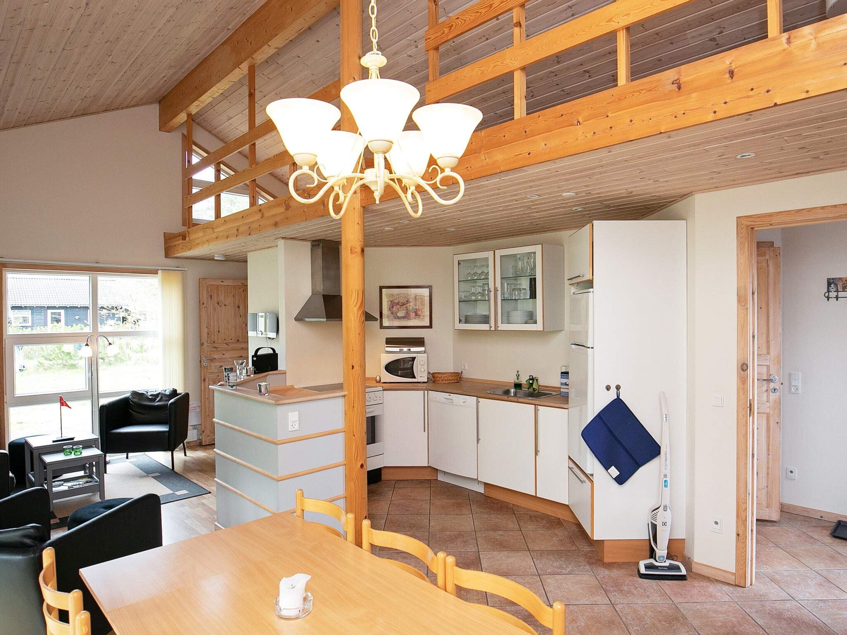 A spacious kitchen with wooden beams, a dining area with a table and chairs, and a view of the outside through large windows.