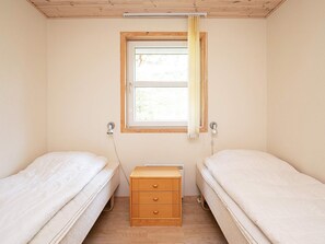 A small, single-room accommodation with two beds, a window with curtains, a wooden cabinet, and a radiator.