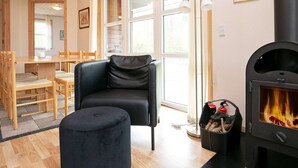 A cozy living room with a black leather sofa, a round ottoman, a wooden dining table with chairs, and a black wood-burning stove. - 6 Person Holiday Home in Laeso (Læsø)