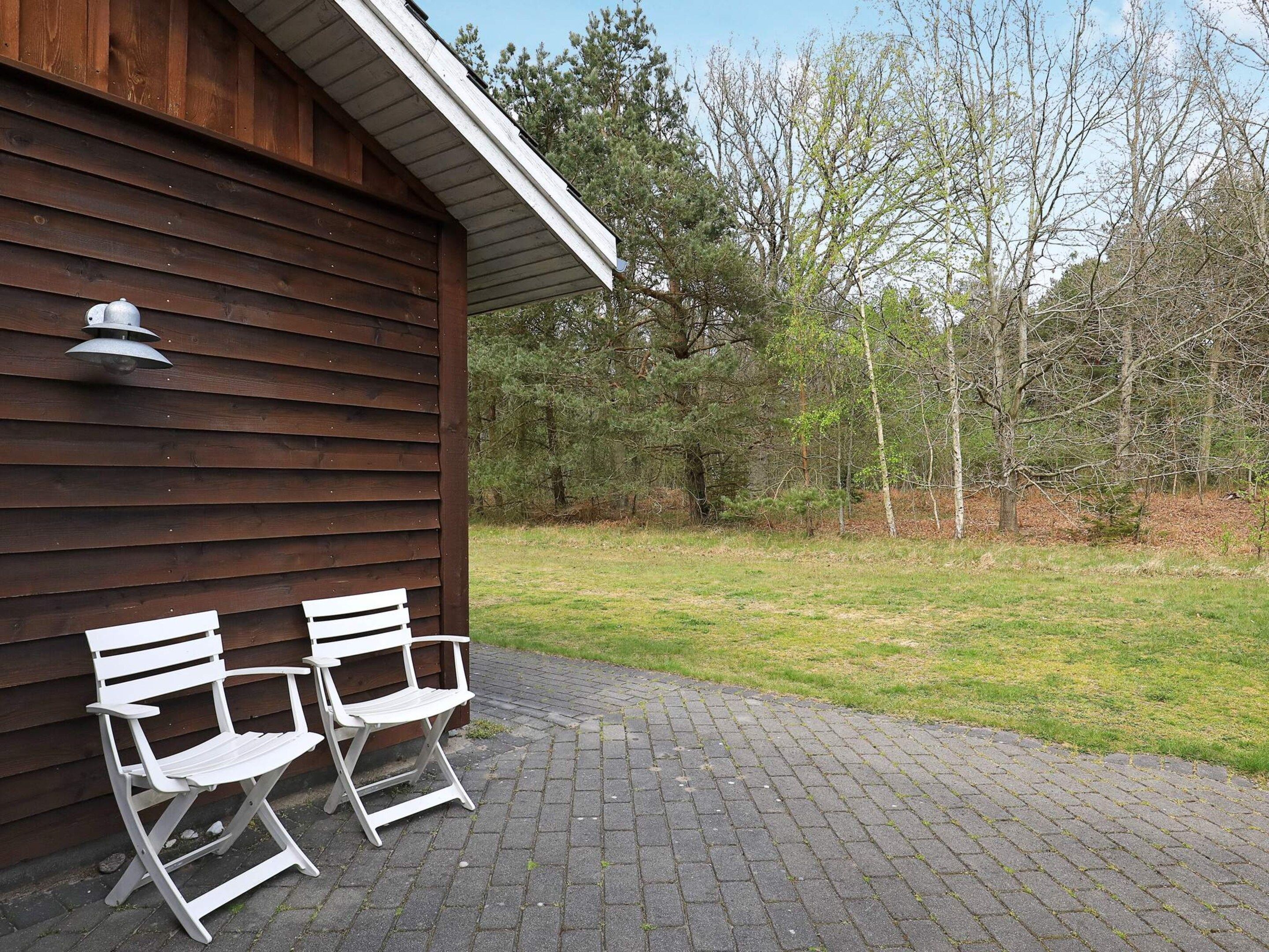 A wooden building with two white folding chairs outside on a paved area.