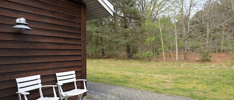 A wooden building with two white folding chairs outside on a paved area.
