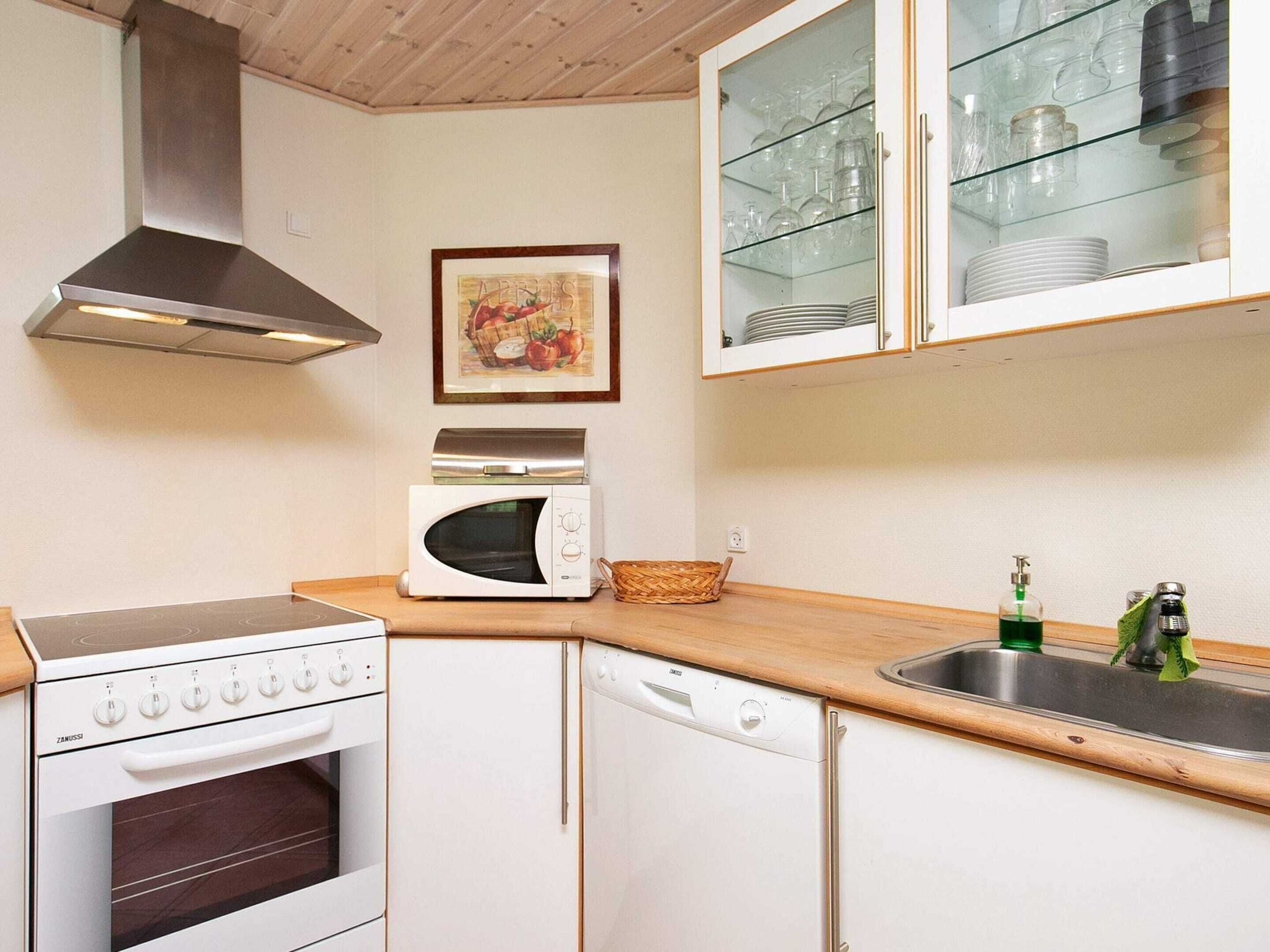 A compact kitchen with a stove, microwave, and dishwasher, a wooden countertop, and a glass cabinet above the sink.