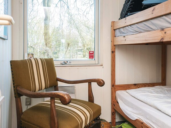 A bunk bed with a window, a chair with a striped cushion, and a visible alarm clock.