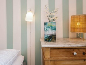 Une chambre avec un lit, une table de chevet avec une lampe, un vase de fleurs et un livre intitulé « Fejltrin » de Maria Adolfsson.