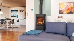 Ein gemütliches Wohnzimmer mit einer Couch, einem Tisch mit zwei Tassen, einem Kamin, einem Essbereich mit Stühlen und einer Küche im Hintergrund.