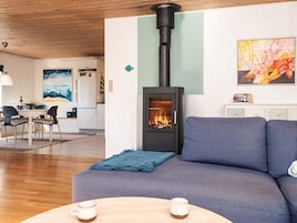 Una sala de estar acogedora con un sofá, una mesa con dos tazas, una chimenea, una zona de comedor con sillas y una cocina al fondo.