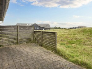 A paved pathway leading to a wooden gate, with a grassy field and buildings in the background. - Scenic Holiday Home in Harboøre near Sea (Harboore)