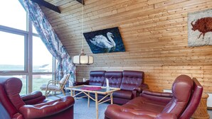 Ein gemütliches Wohnzimmer mit Holzboden, einem großen Fenster und Blick ins Freie.