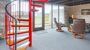 Ein modernes Interieur mit einer Wendeltreppe, Blick durch große Fenster und einer Sitzecke mit Tisch und Stühlen.