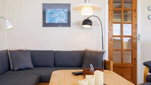 Un salon moderne avec un canapé gris, une table basse en bois ornée de bougies, une télécommande et un tableau abstrait encadré accroché au mur.
