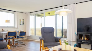 Un salon chaleureux avec une cheminée, un coin repas avec des chaises et une grande fenêtre donnant sur un beau paysage.