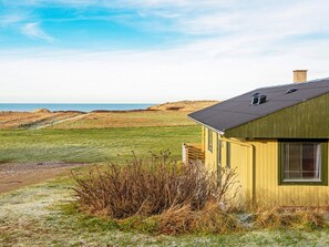 A coastal house with a green roof, a visible chimney, and a view of the sea.