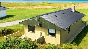 Une maison de plain-pied avec un toit sombre, de grandes fenêtres et une vue sur la mer.
