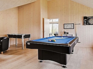 A pool table with balls, a foosball table, and dartboards in a room with wooden walls and a sloped ceiling.