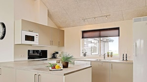 Una cocina moderna con una isla central, electrodomésticos integrados y un ventanal con persianas.