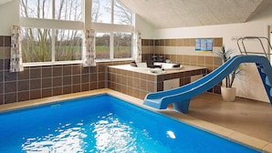 Una piscina interior con tobogán, una ventana con cortinas y un mostrador con lavabo.