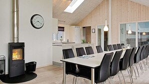 Un comedor moderno con una mesa larga, sillas, una estufa de leña y un reloj en la pared.