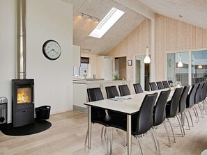 Un espace de repas moderne avec une longue table, des chaises, un poêle à bois et une horloge au mur.