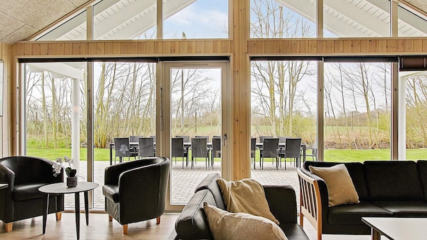 Amplio espacio interior con grandes ventanales, mobiliario de madera y vistas a un área verde al aire libre.