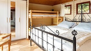 Quarto de cabana de madeira com uma cama beliche, um guarda-roupa branco e uma mesa de madeira.