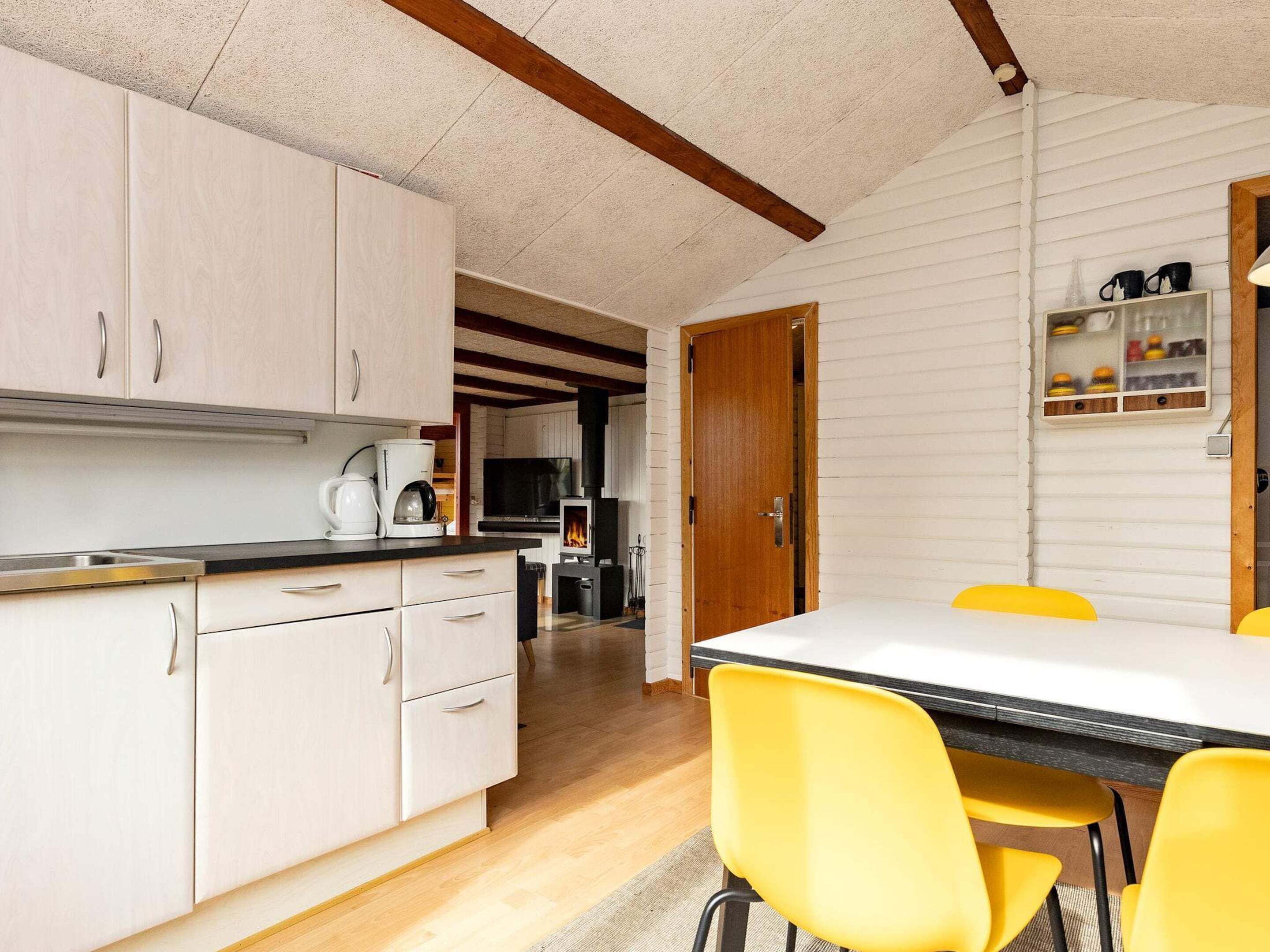 A compact kitchen with white cabinets, a coffee maker, and a dining table with yellow chairs.