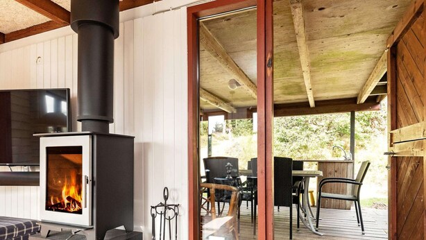 Uma cabana acolhedora com lareira a lenha, porta de vidro que dá para um deck externo e área de refeições com mobiliário de exterior.