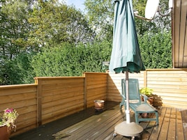 Una terraza de madera con un paraguas verde, una silla y plantas en macetas.