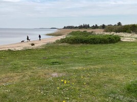 Paisagem costeira com uma praia de areia, áreas com grama e um corpo d'água.