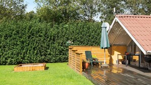 En træterrasse med et overdækket siddeområde, et træskur og en velplejet græsplæne.