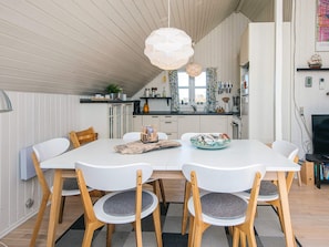 A modern kitchen with white cabinetry, a dining table with chairs, and a hanging light fixture. - Modish Holiday Home in Jutland near Sea (Harboore)