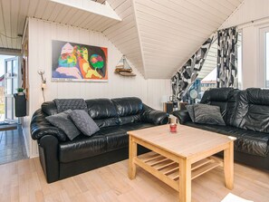 A modern living room with a black leather sofa, a wooden coffee table, and a colorful abstract painting on the wall. - Modish Holiday Home in Jutland near Sea (Harboore)