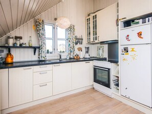 A kitchen with white cabinets, a black countertop, a stove, an oven, a refrigerator, and a window with curtains. - Modish Holiday Home in Jutland near Sea (Harboore)