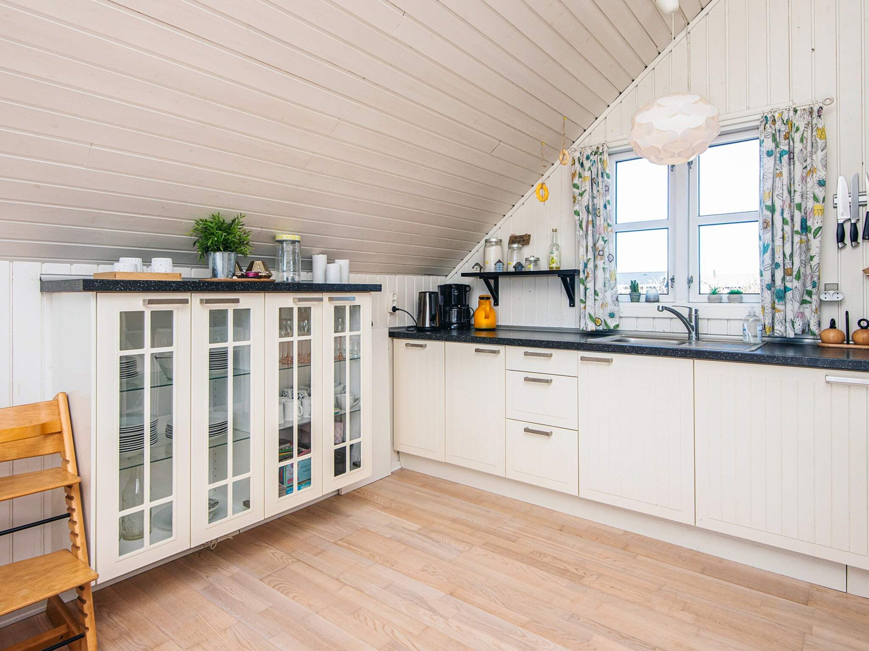 Una cocina con armarios blancos, encimera de madera y una ventana con cortinas.