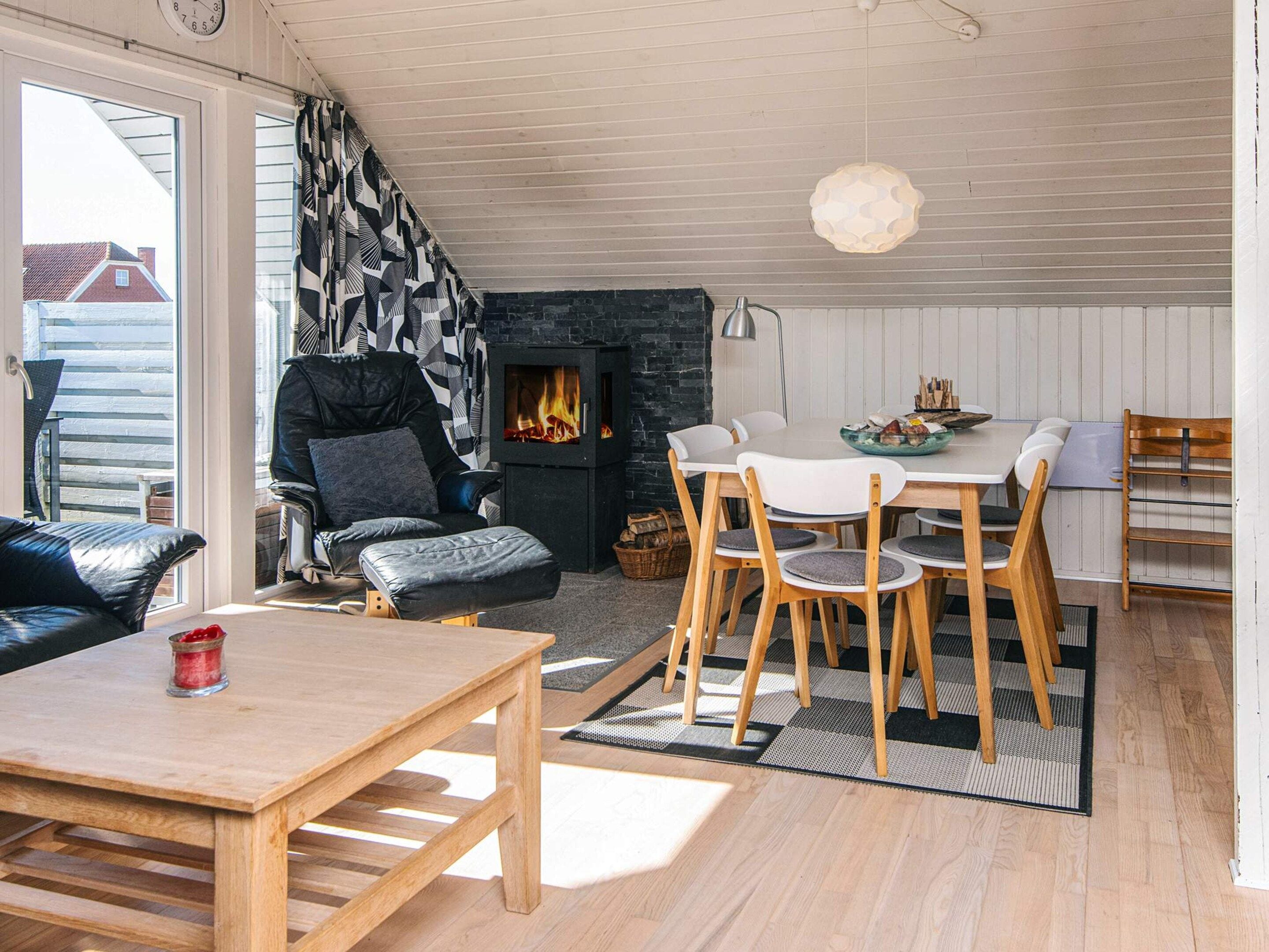 Una sala de estar acogedora con chimenea, un comedor con sillas de madera y un sofá con un plaid blanco y negro.