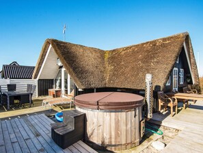 A wooden deck with a hot tub, outdoor seating, and a thatched-roof structure. - Modish Holiday Home in Jutland near Sea (Harboore)