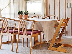 A dining area with a table covered by a tablecloth, surrounded by wooden chairs with cushions.