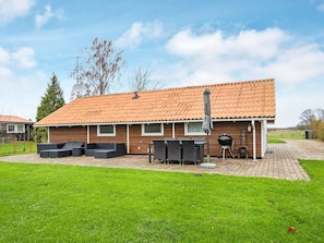 A house with a tiled roof, a patio with outdoor furniture, and a barbecue grill.