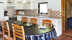 Een kleine keuken met witte kastjes, een fornuis, een magnetron en een spoelbak. Er is een eettafel met stoelen en een kroonluchter erboven.