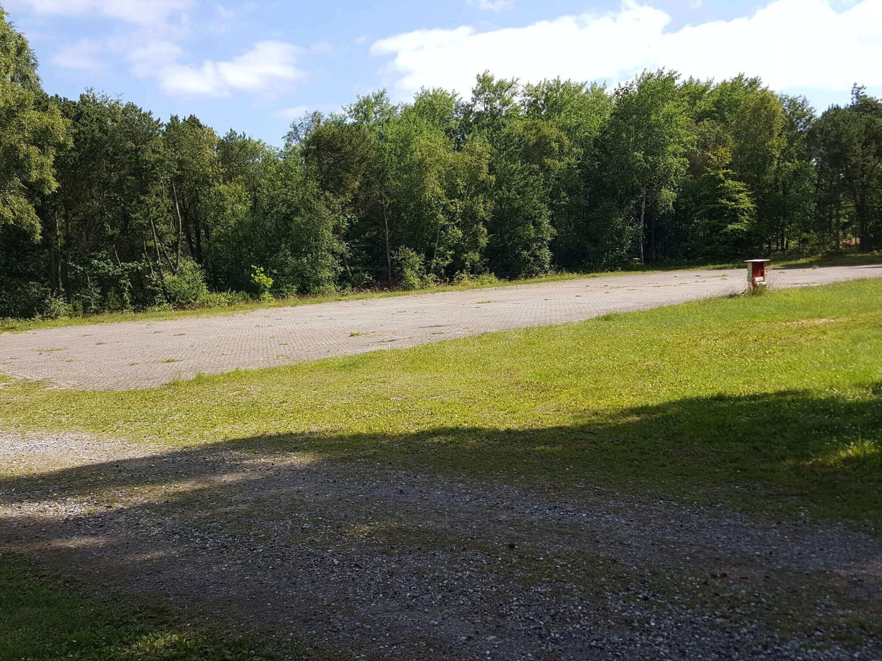 A gravel parking area with a paved path leading to a red mailbox.