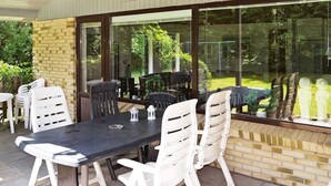 Een terras buiten met een tafel en stoelen, grote ramen en een bakstenen muur.