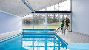An indoor swimming pool with clear glass walls, a tiled floor, and a view of trees outside. - 5 Star Holiday Home in Hadsund (Hadsund)