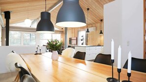 A modern dining area with a wooden table, black pendant lights, and white candles. - 5 Star Holiday Home in Hadsund (Hadsund)