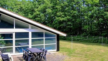 En moderne bygning med store vinduer og en overdækket patio med udendørs siddepladser.