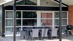 A covered patio with a table and chairs, large windows, and a grill. - 5 Star Holiday Home in Hadsund (Hadsund)