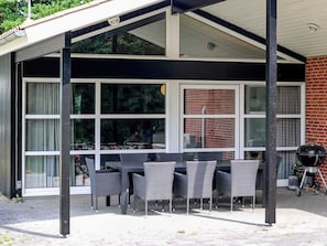 A covered patio with a table and chairs, large windows, and a grill. - 5 Star Holiday Home in Hadsund (Hadsund)