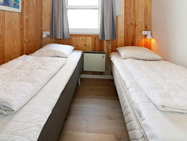 Una habitación con dos camas, una ventana con cortinas y un calentador fijado a la pared.